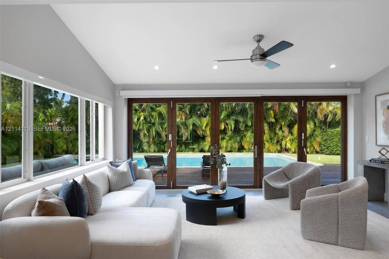 5386 Alton Road, Miami Beach, FL 33140 Vaulted ceilings featuring recessed lighting, a modern ceiling fan, expansive multi-panel sliding glass doors, and large windows encompassing exterior pool and landscape elements