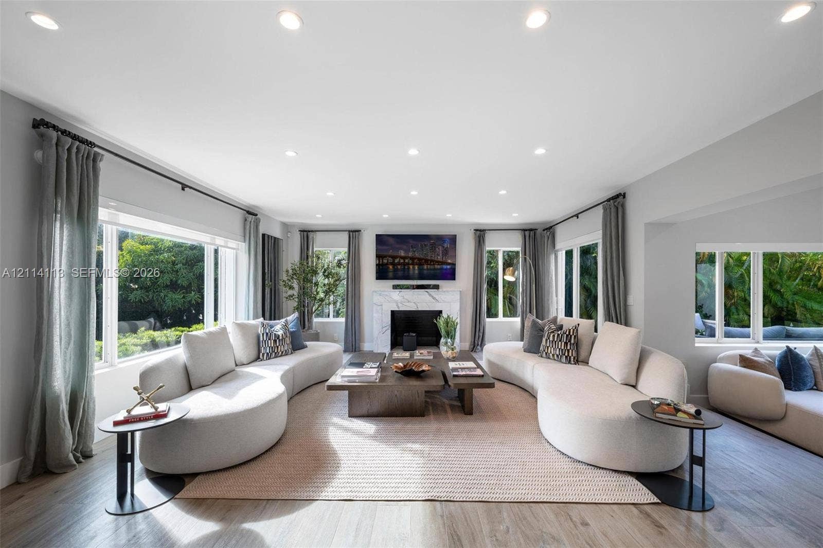 5386 Alton Road, Miami Beach, FL 33140 Living area featuring wood-finish flooring, recessed lighting, expansive multi-pane windows, and a central fireplace with a stone-finish surround