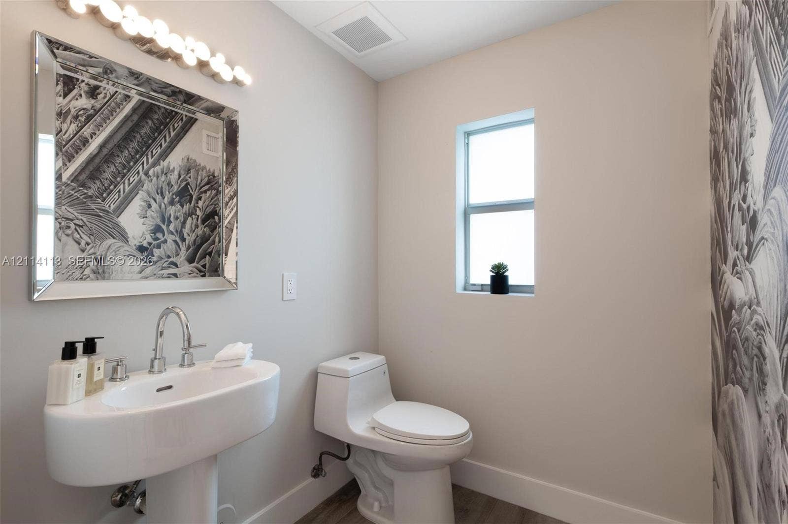 5386 Alton Road, Miami Beach, FL 33140 Pedestal sink with chrome faucet, multi-bulb vanity light, framed mirror, and toilet featuring a modern low-profile design