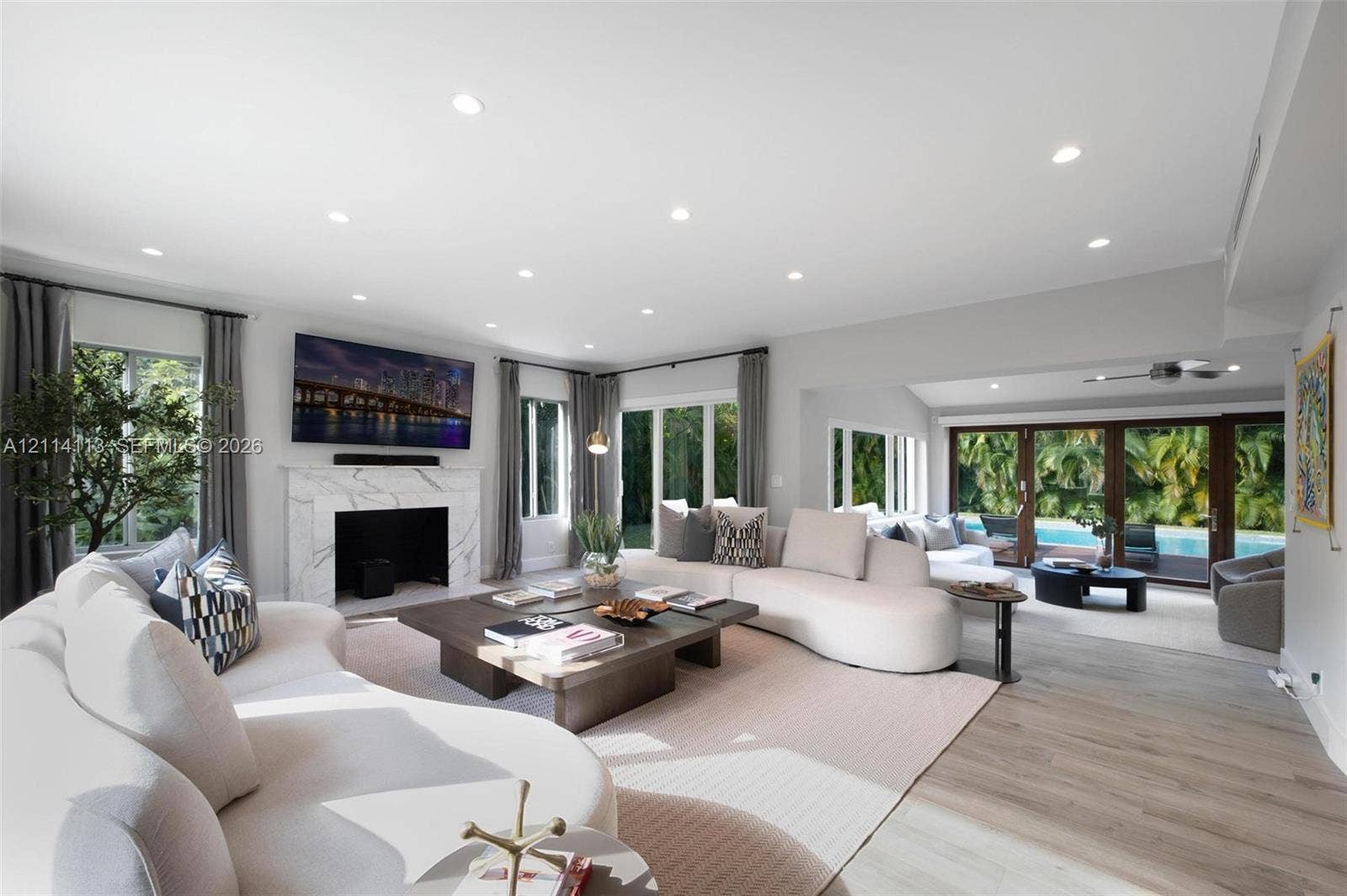 5386 Alton Road, Miami Beach, FL 33140 Open-concept living space featuring wood-finish flooring, recessed lighting, a stone-surround fireplace, and multi-panel glass doors