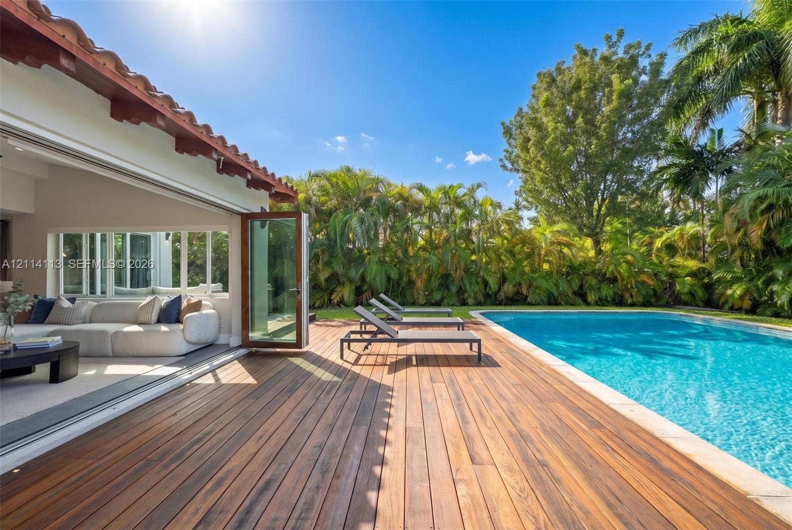 5386 Alton Road, Miami Beach, FL 33140 Rear exterior featuring a wood-finish deck, swimming pool, and wide-opening glass panel doors