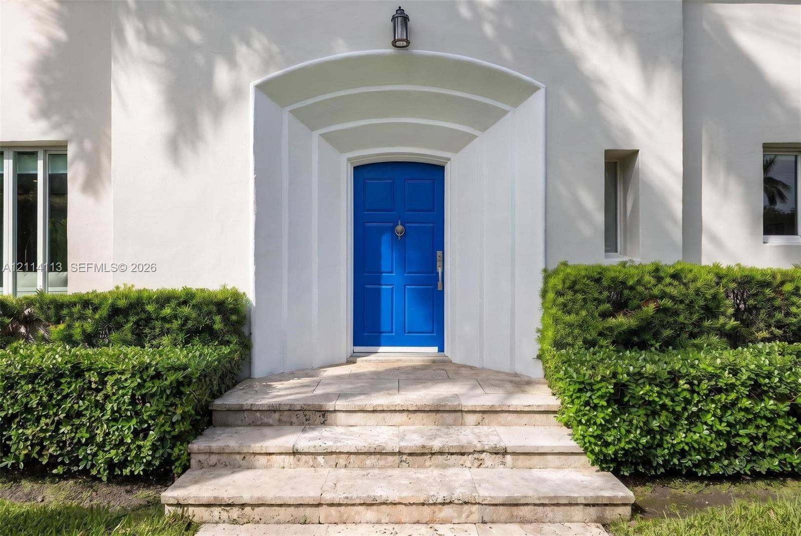 5386 Alton Road, Miami Beach, FL 33140 Stucco exterior entrance featuring an arched recessed doorway, paneled front door, stone steps, and manicured shrubbery