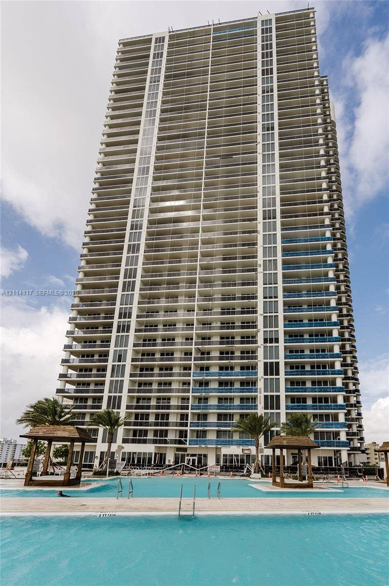 1850 S Ocean Drive, #4008, Hallandale Beach, Hallandale Beach, FL 33009 High-rise condominium tower featuring glass balcony railings, extensive fenestration, and a multi-section swimming pool with integrated sun decks and wooden cabanas