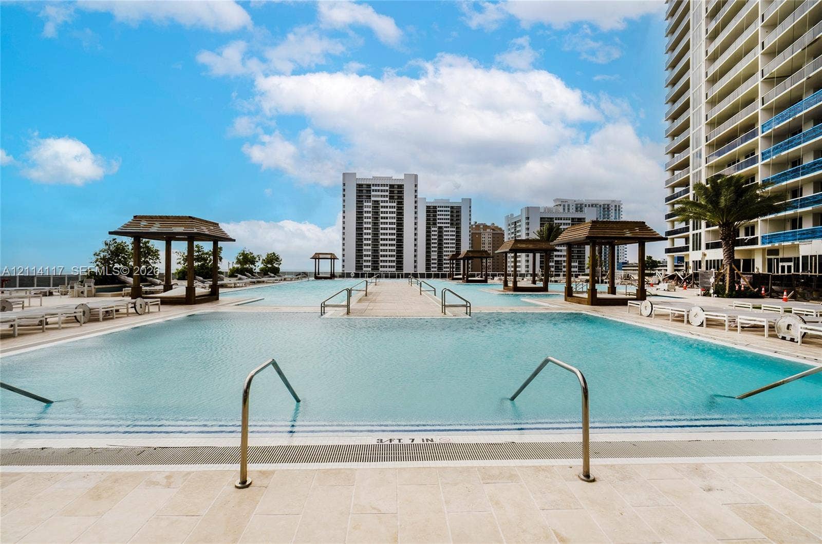 1850 S Ocean Drive, #4008, Hallandale Beach, Hallandale Beach, FL 33009 Large outdoor swimming pool with submerged entry steps, stainless steel handrails, tiled pool deck, and multiple wooden cabana structures