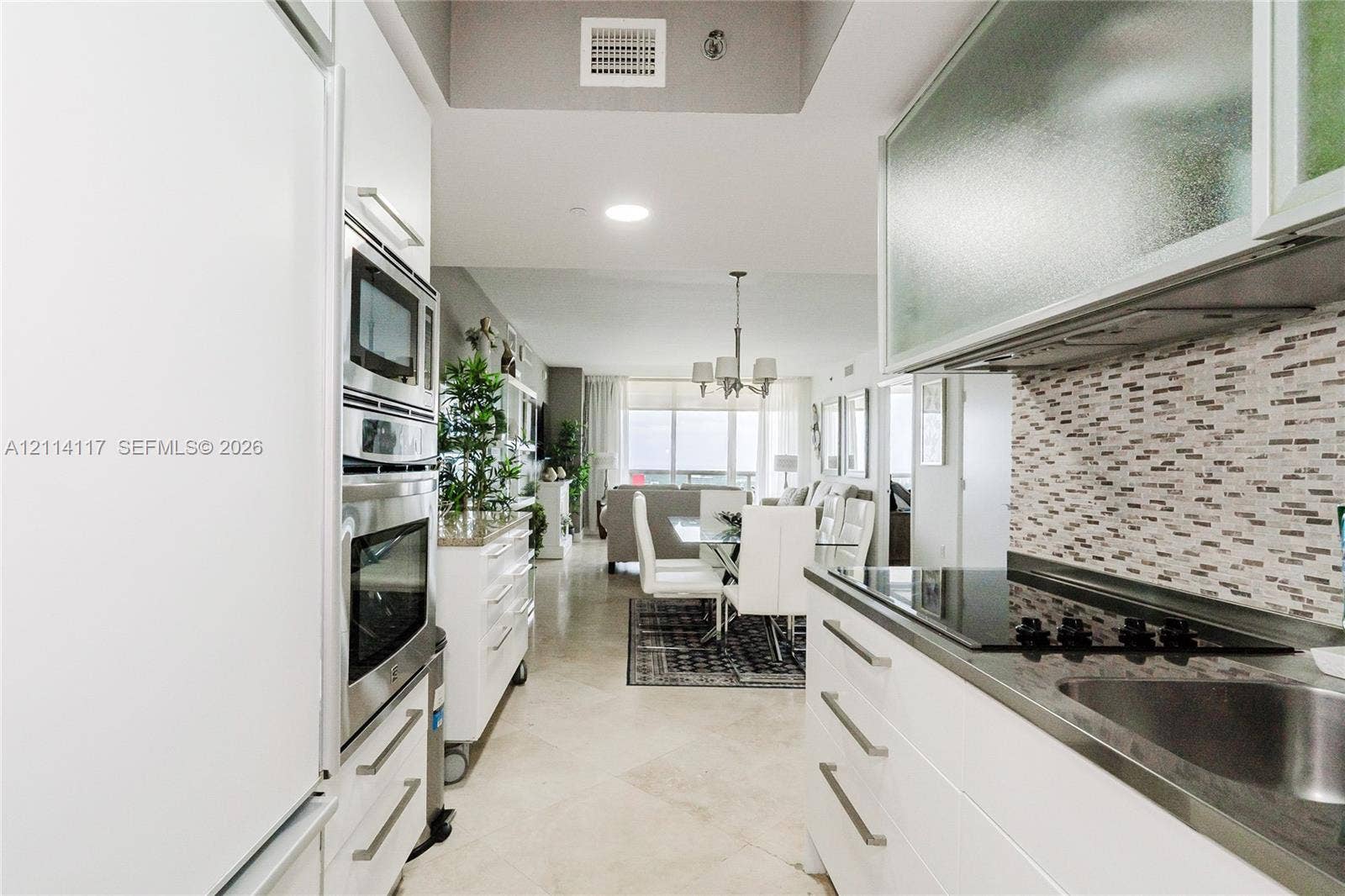 1850 S Ocean Drive, #4008, Hallandale Beach, Hallandale Beach, FL 33009 Galley kitchen featuring white flat-panel cabinetry, stainless steel wall-mounted oven and microwave, mosaic tile backsplash, and stone flooring