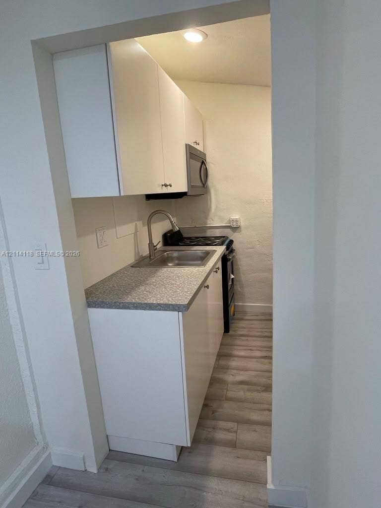 2484 SW 10th Street, #4 - eff, Miami, Miami, FL 33135 Kitchen featuring white cabinetry, stone-finish countertops, stainless steel sink with gooseneck faucet, integrated microwave, and wood-finish flooring