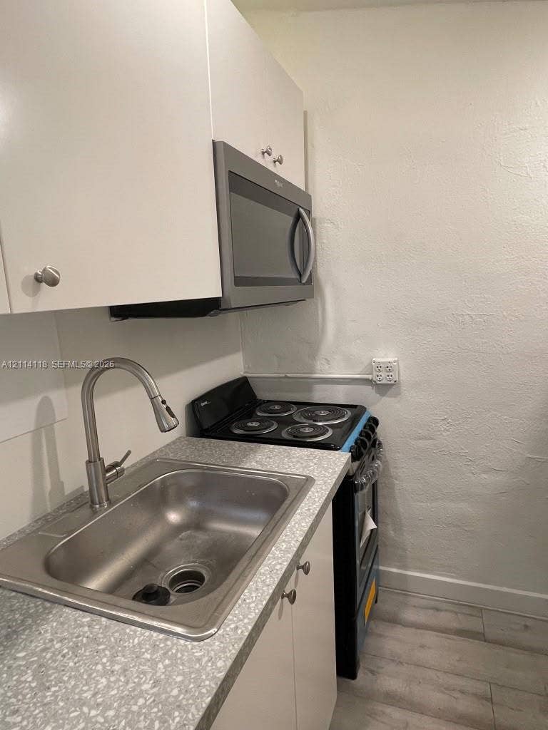 2484 SW 10th Street, #4 - eff, Miami, Miami, FL 33135 Kitchen featuring white cabinetry, a stainless steel sink with an arched pull-down faucet, a textured countertop, and a built-in microwave oven