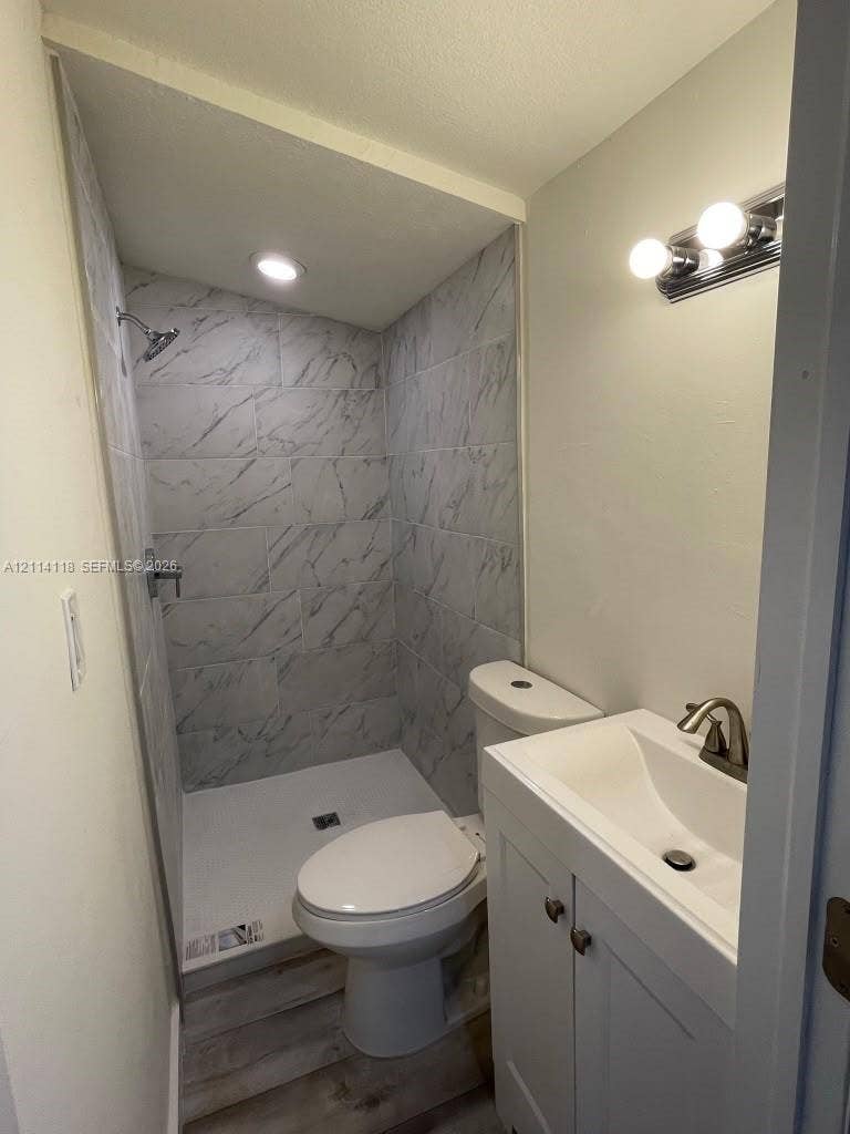 2484 SW 10th Street, #4 - eff, Miami, Miami, FL 33135 Bathroom featuring a shower stall with stone-patterned wall tile, white vanity cabinet with a integrated sink, polished metal hardware, wood-finish flooring, and wall-mounted vanity lighting