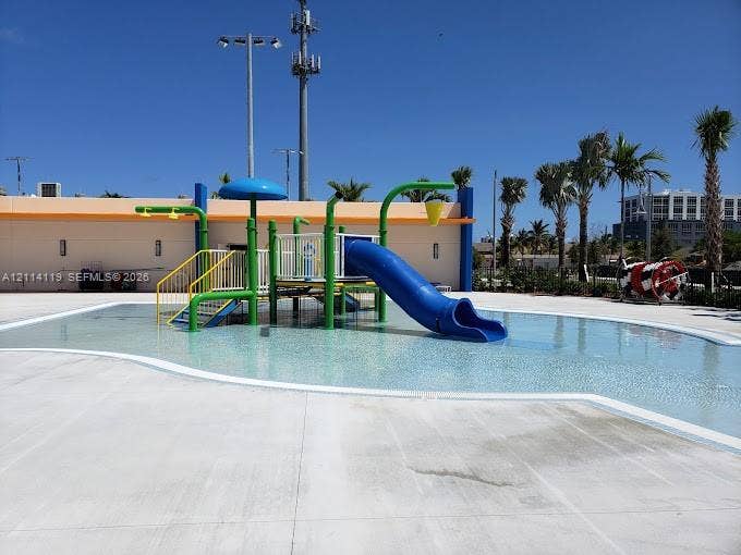 Water play area featuring a shallow-entry pool, integrated structure with a slide, overhead water features, and concrete decking