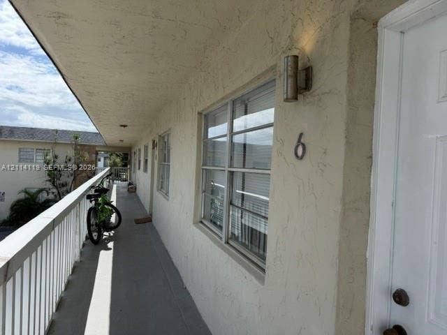 Exterior walkway featuring a textured stucco facade, metal railing, and cylindrical wall-mounted exterior lighting