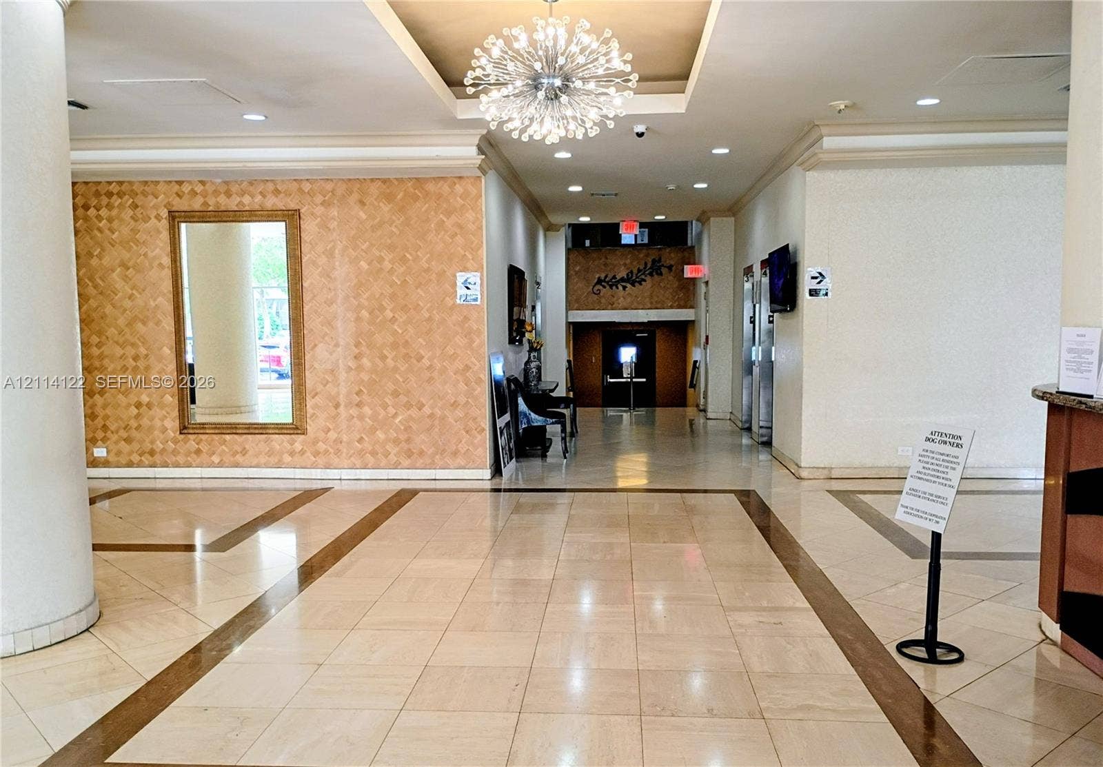 251 174th Street, #1208, Sunny Isles Beach, Sunny Isles Beach, FL 33160 Lobby area featuring polished tile flooring with inlaid borders, a decorative recessed ceiling with a contemporary chandelier, and a textured accent wall