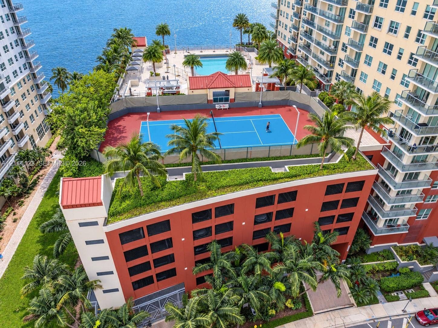 1155 Brickell Bay Drive, #2609, Miami, FL 33131 Rooftop amenities featuring a tennis court, swimming pool, mature palm trees, and waterfront perimeter