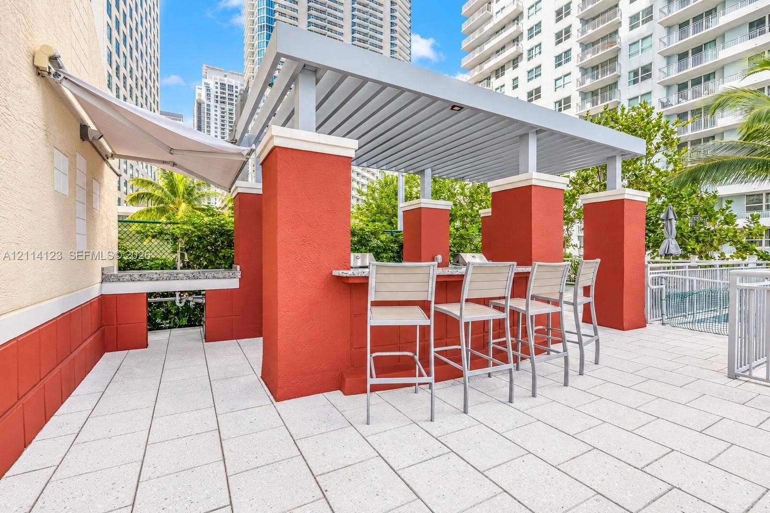1155 Brickell Bay Drive, #2609, Miami, FL 33131 Outdoor kitchen area featuring a built-in stone-surface counter, integrated grill, overhead louvered pergola, and tiled patio flooring