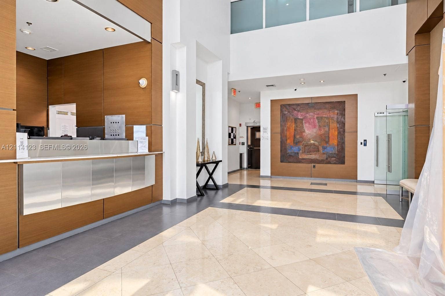 1155 Brickell Bay Drive, #2609, Miami, FL 33131 Lobby featuring double-height ceilings, wood-finish paneling, stone-tile flooring with decorative inlays, and a stainless steel reception desk
