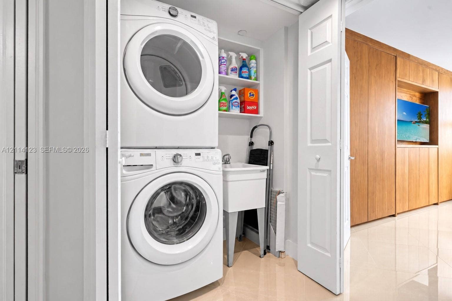 1155 Brickell Bay Drive, #2609, Miami, FL 33131 Laundry closet featuring a stacked front-load washer and dryer, utility sink, overhead shelving, and floor-to-ceiling wood-finish cabinetry