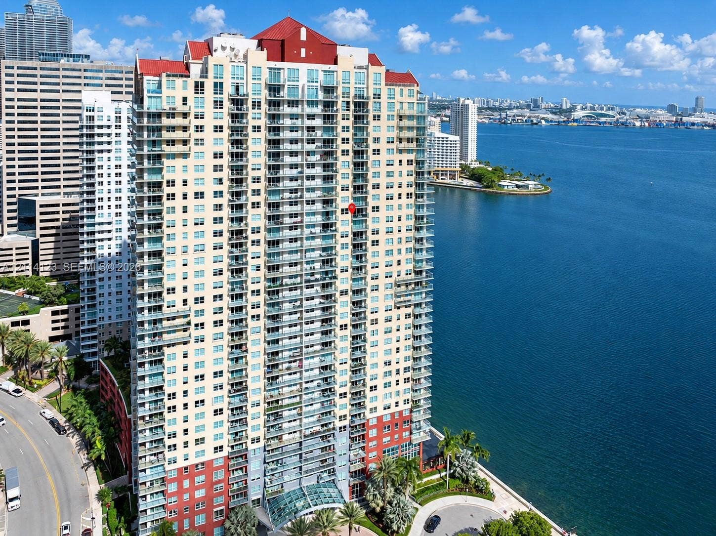 1155 Brickell Bay Drive, #2609, Miami, FL 33131 High-rise residential tower featuring a glass facade, multiple levels of private balconies, a distinctive red peaked roof, and direct waterfront placement