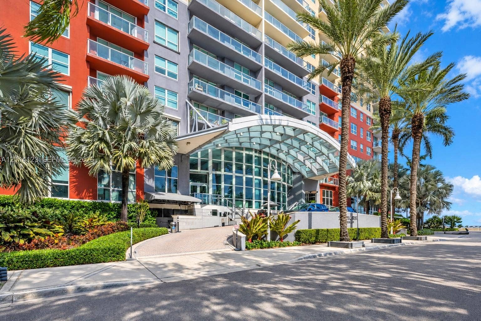 1155 Brickell Bay Drive, #2609, Miami, FL 33131 High-rise exterior featuring a glass-canopied entryway, floor-to-ceiling windows, private balconies with glass railings, and mature palm tree landscaping