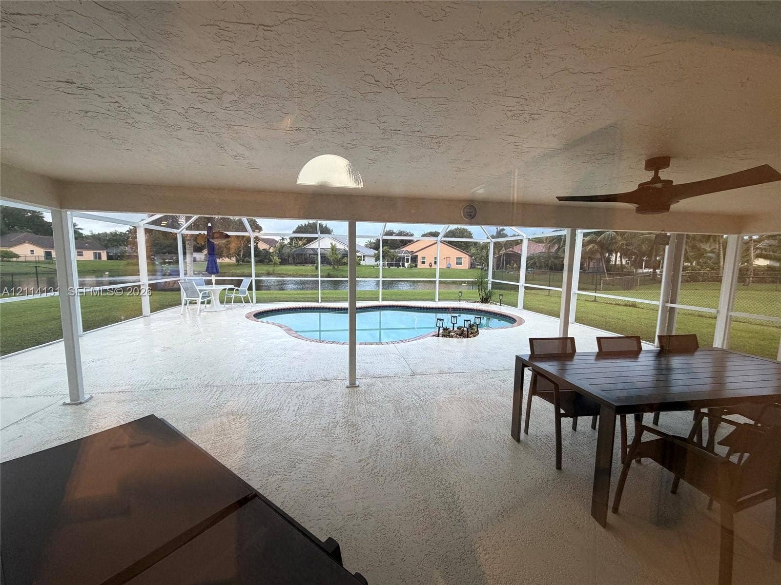 9012 Southern Orchard Road N, Davie, FL 33328 Screened-in lanai featuring a concrete patio, built-in ceiling fan, and kidney-shaped pool overlooking the water
