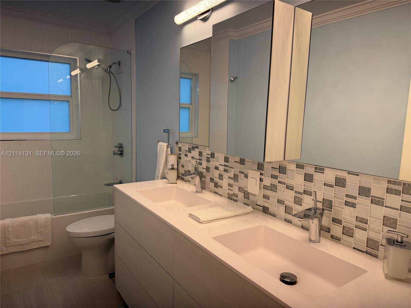 9012 Southern Orchard Road N, Davie, FL 33328 Double vanity with an integrated countertop, rectangular vessel sinks, chrome fixtures, mosaic tile backsplash, and wall-mounted medicine cabinets