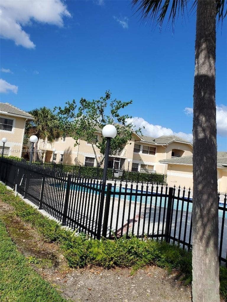 12143 Royal Palm Boulevard, #8E, Coral Springs, Coral Springs, FL 33065 Swimming pool area featuring a perimeter black metal fence, integrated pole lighting, and manicured landscaping