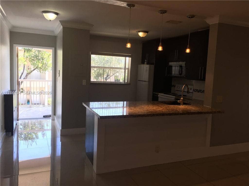 12143 Royal Palm Boulevard, #8E, Coral Springs, Coral Springs, FL 33065 Kitchen featuring a breakfast bar, dark-finish cabinetry, tile flooring, pendant lighting, and a doorway providing access to a balcony