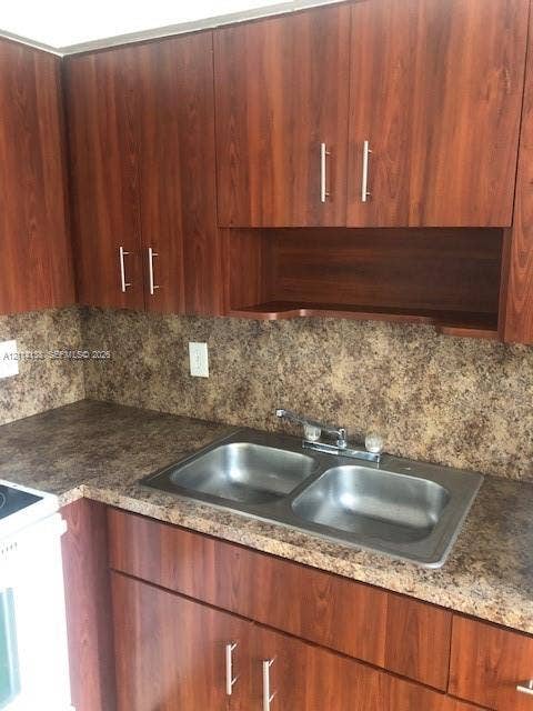2323 Scott Street, #Front, Hollywood, Hollywood, FL 33020 Wood-finish cabinetry with silver-tone pulls, integrated open shelving, speckled laminate countertop, and a stainless steel double-basin sink with a dual-handle faucet