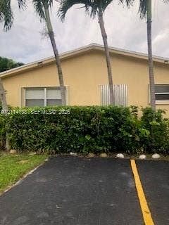 2323 Scott Street, #Front, Hollywood, Hollywood, FL 33020 Stucco exterior featuring a gabled roofline, mature palm trees, and landscaped hedging, set alongside an asphalt parking surface