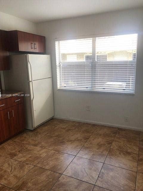 2323 Scott Street, #Front, Hollywood, Hollywood, FL 33020 Kitchen featuring wood-finish cabinetry, stone-texture laminate countertops, large-format tile flooring, and a window with horizontal blinds
