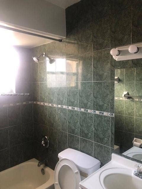 2323 Scott Street, #Front, Hollywood, Hollywood, FL 33020 Bathroom featuring full-height green ceramic wall tiling with a decorative mosaic border, a built-in bathtub, a white vanity with an integrated sink, and a dual-bulb vanity light fixture