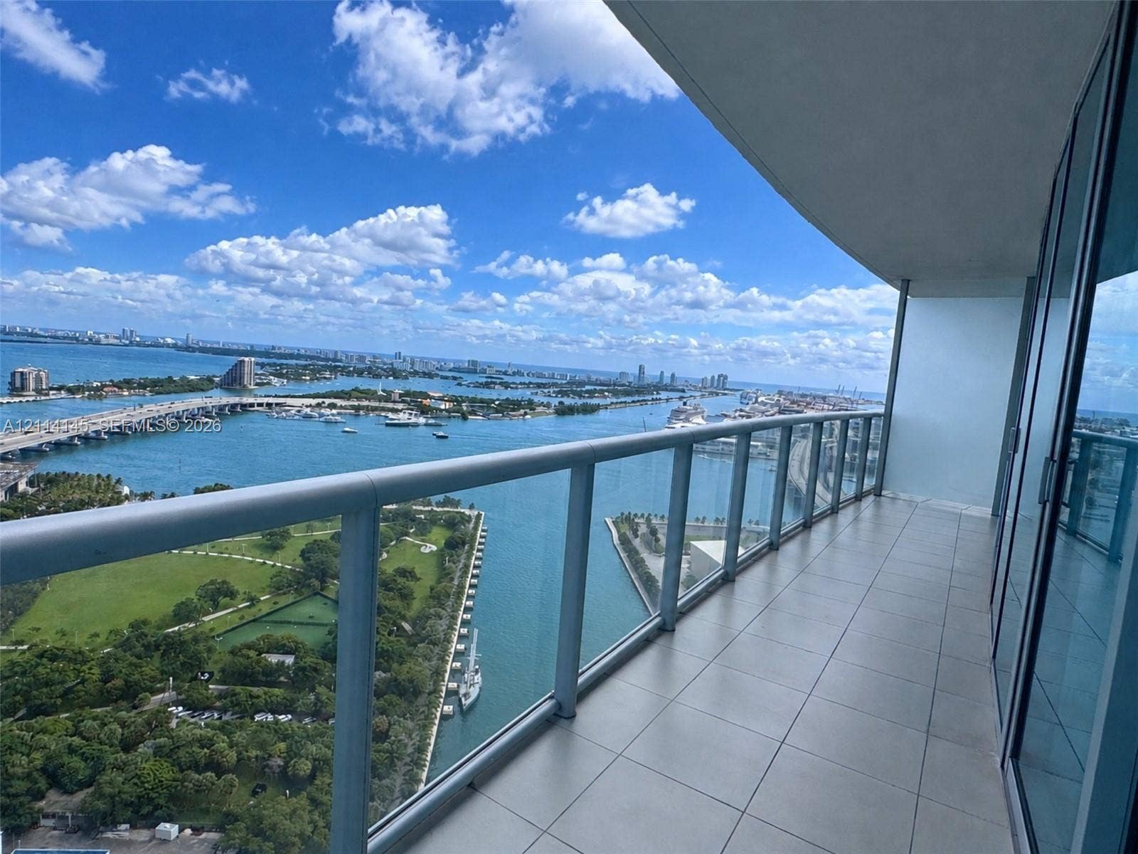 Expansive balcony with large-format tile flooring and a minimalist glass-paneled railing overlooking the bay and surrounding islands