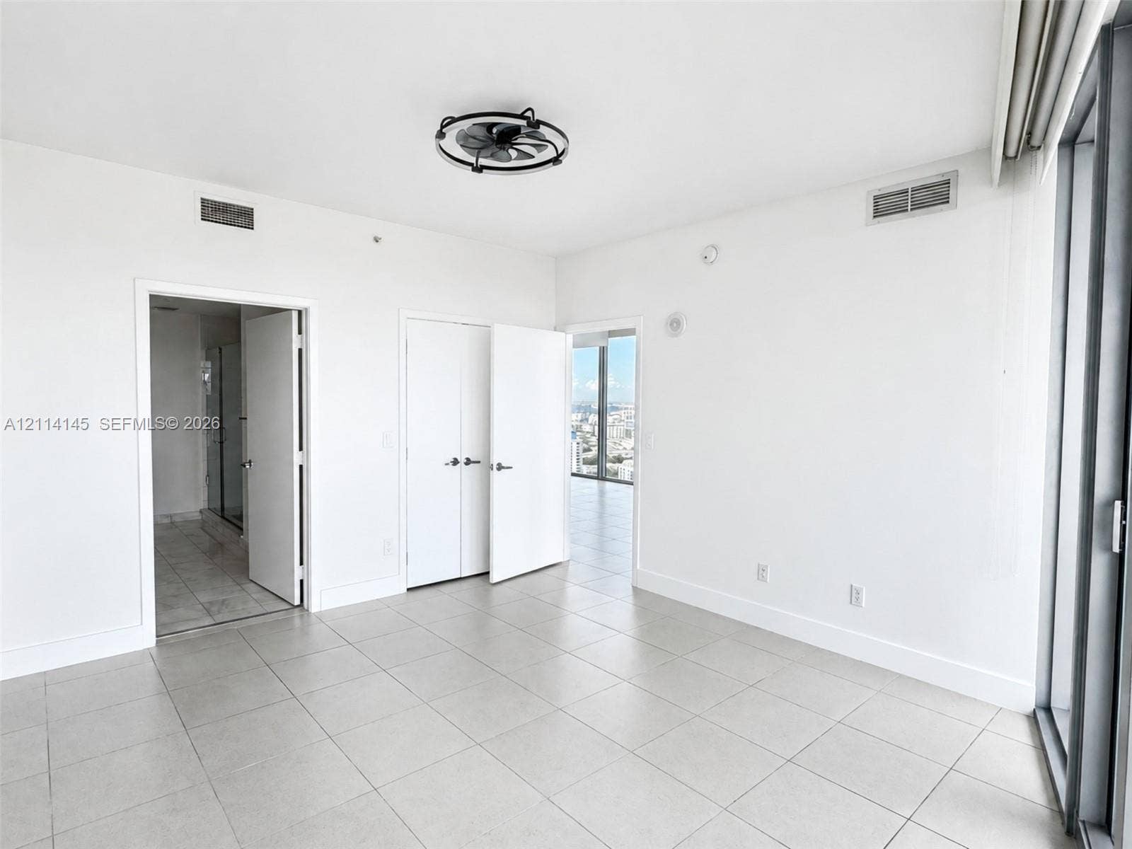 Room featuring large-format tile flooring, a minimalist industrial-style flush-mount ceiling fan, double-door closet cabinetry, and floor-to-ceiling glass paneling