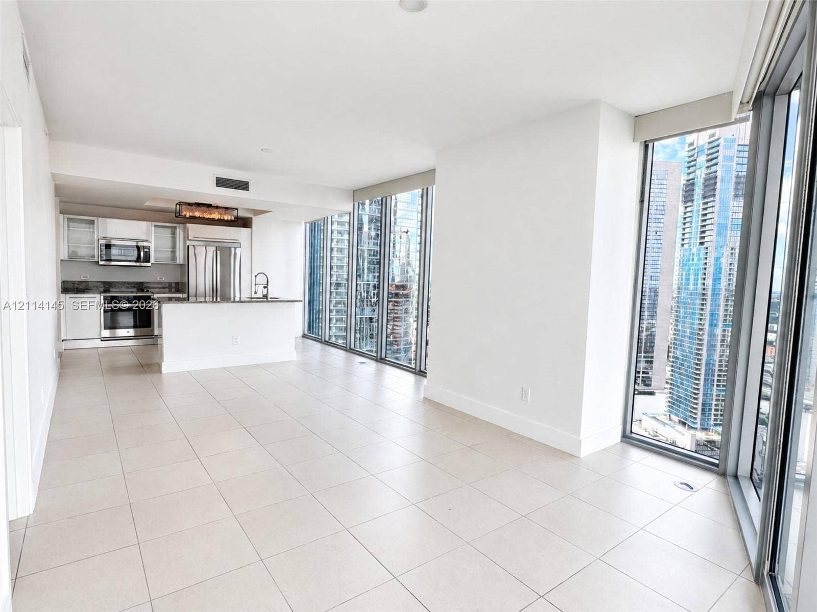Open-concept kitchen featuring stainless steel appliances, white cabinetry, and stone-surface countertops, complemented by floor-to-ceiling windows and tile flooring