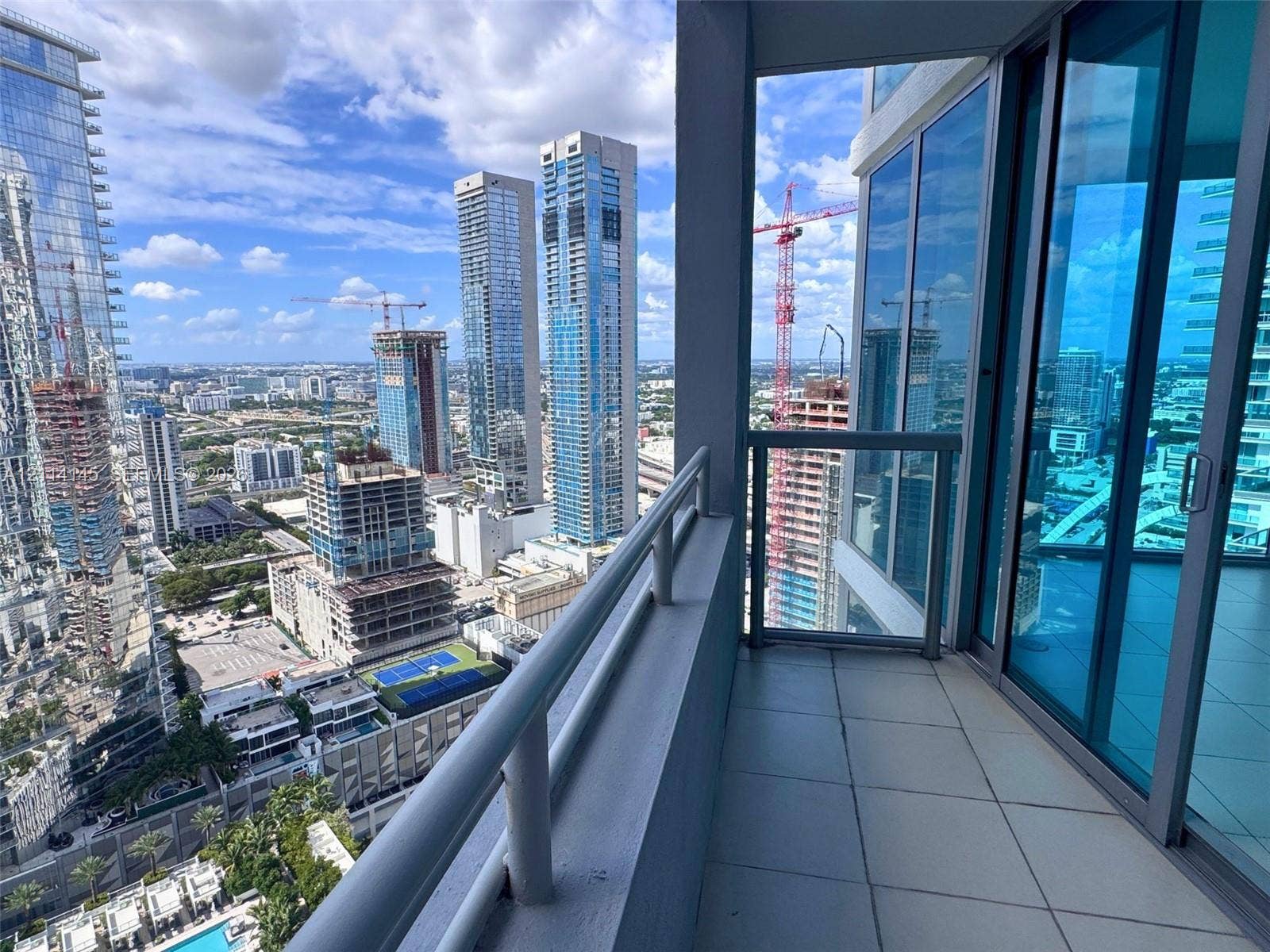 Covered balcony featuring tile flooring and a metal railing, paired with floor-to-ceiling glass panel sliding doors