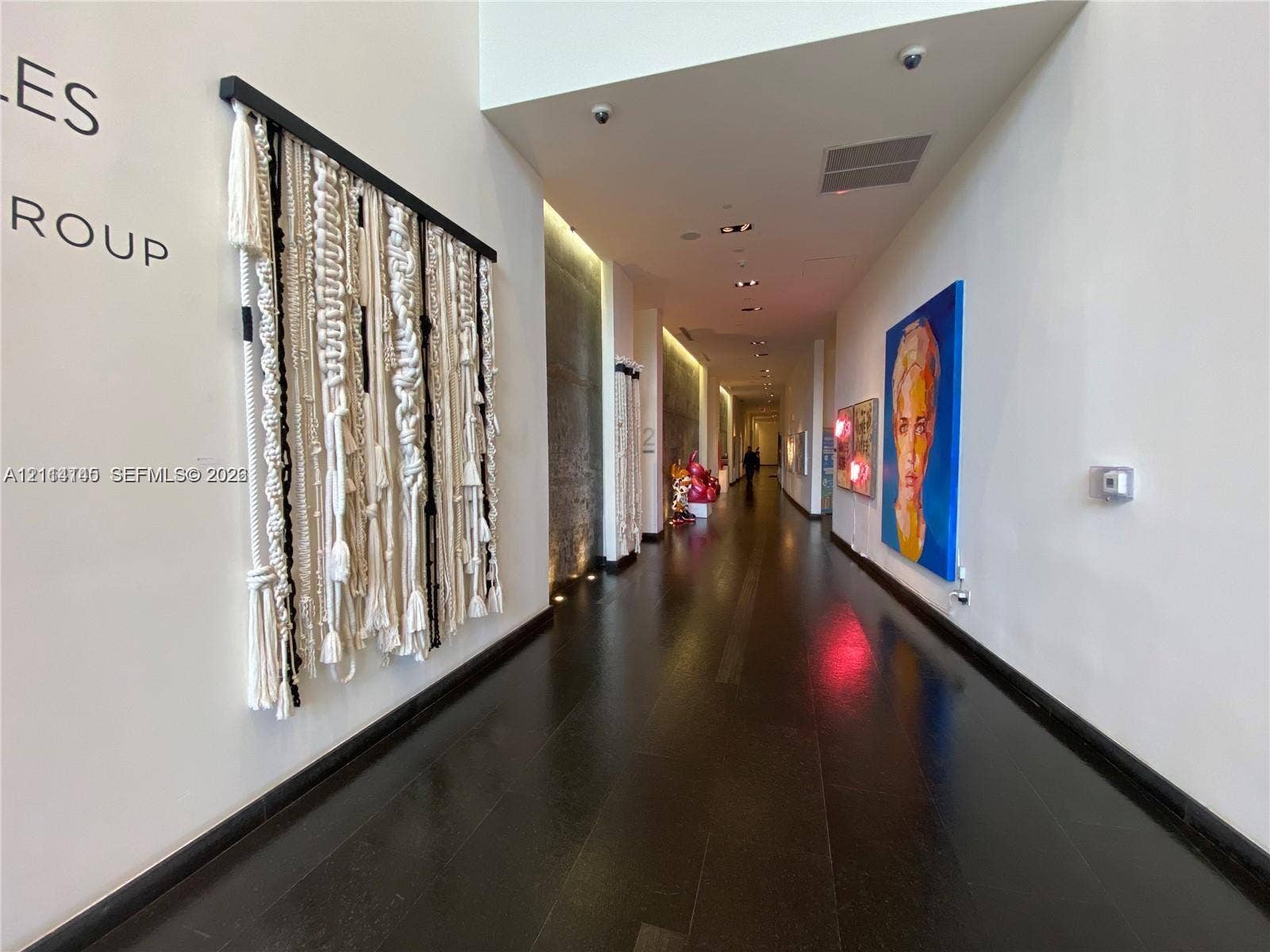 Wide corridor featuring dark wood-finish flooring, high ceilings, integrated recessed lighting, and a floor-to-ceiling textured stone accent wall with built-in uplighting