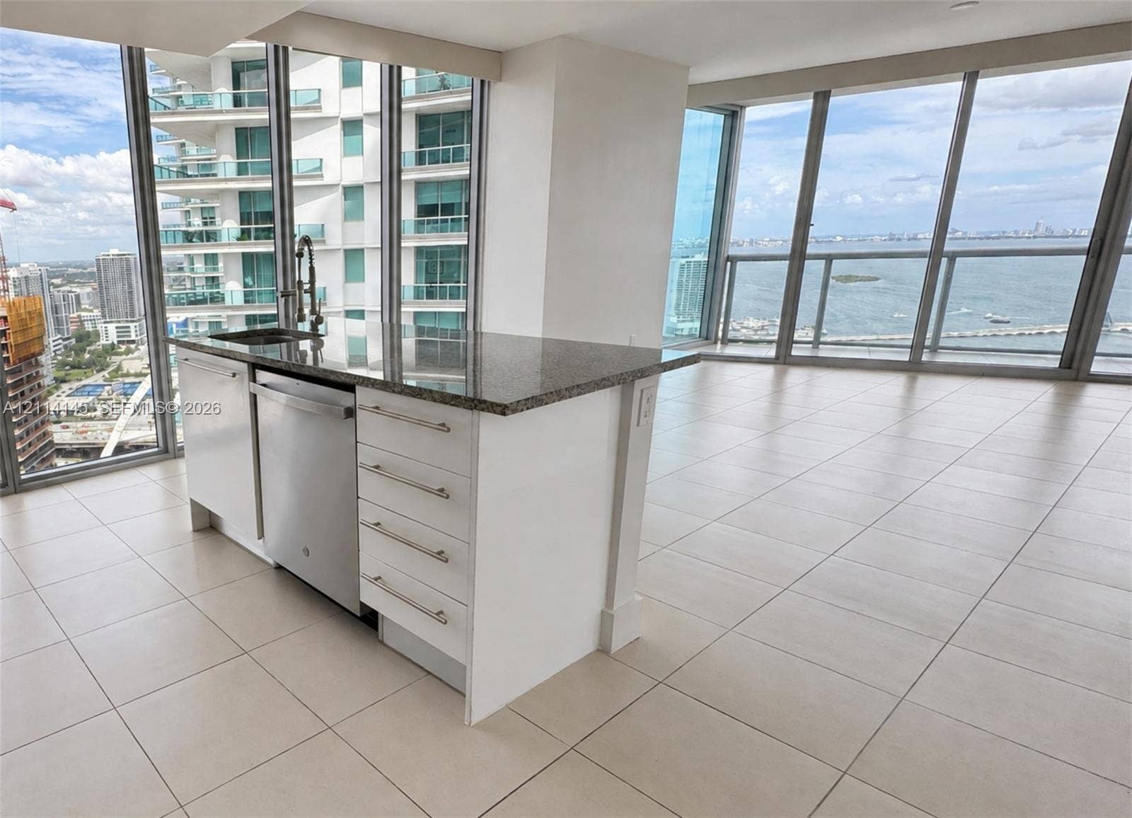 Floor-to-ceiling windows, kitchen island with stone countertop, stainless steel dishwasher, high-rise water backdrop, and large-format tile flooring