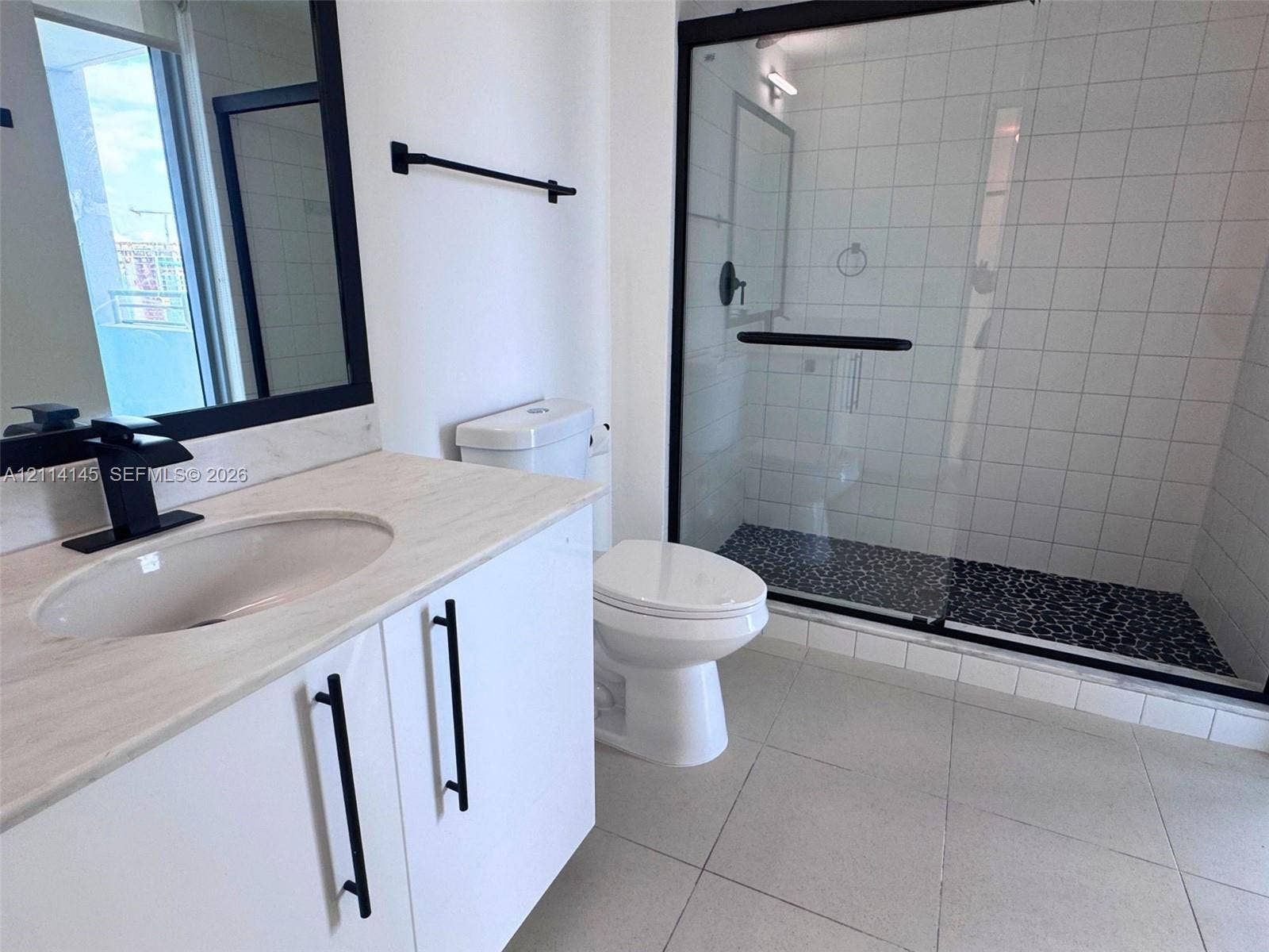 Bathroom featuring a vanity with a light-toned countertop, an integrated sink with a matte black faucet, a walk-in shower with a glass enclosure and pebble-stone flooring, and matte black hardware