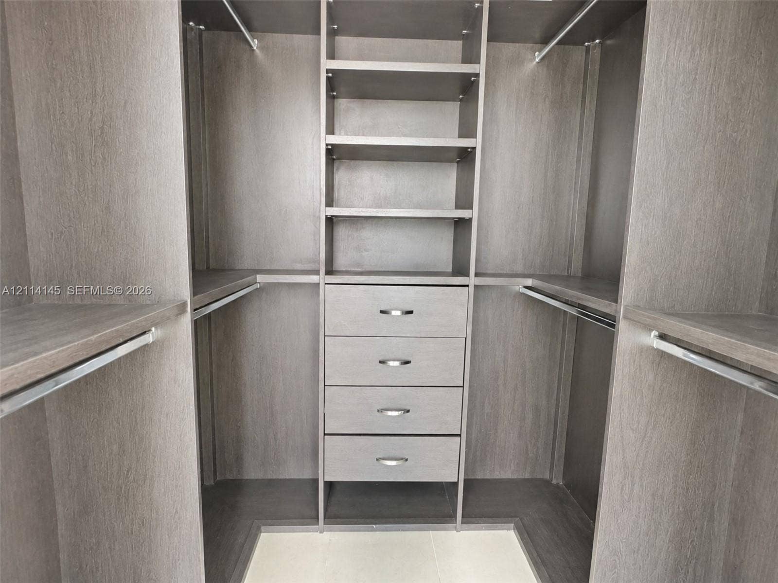 Custom closet organization system featuring wood-finish cabinetry, four integrated storage drawers with brushed metal pulls, adjustable shelving, and multiple hanging rods