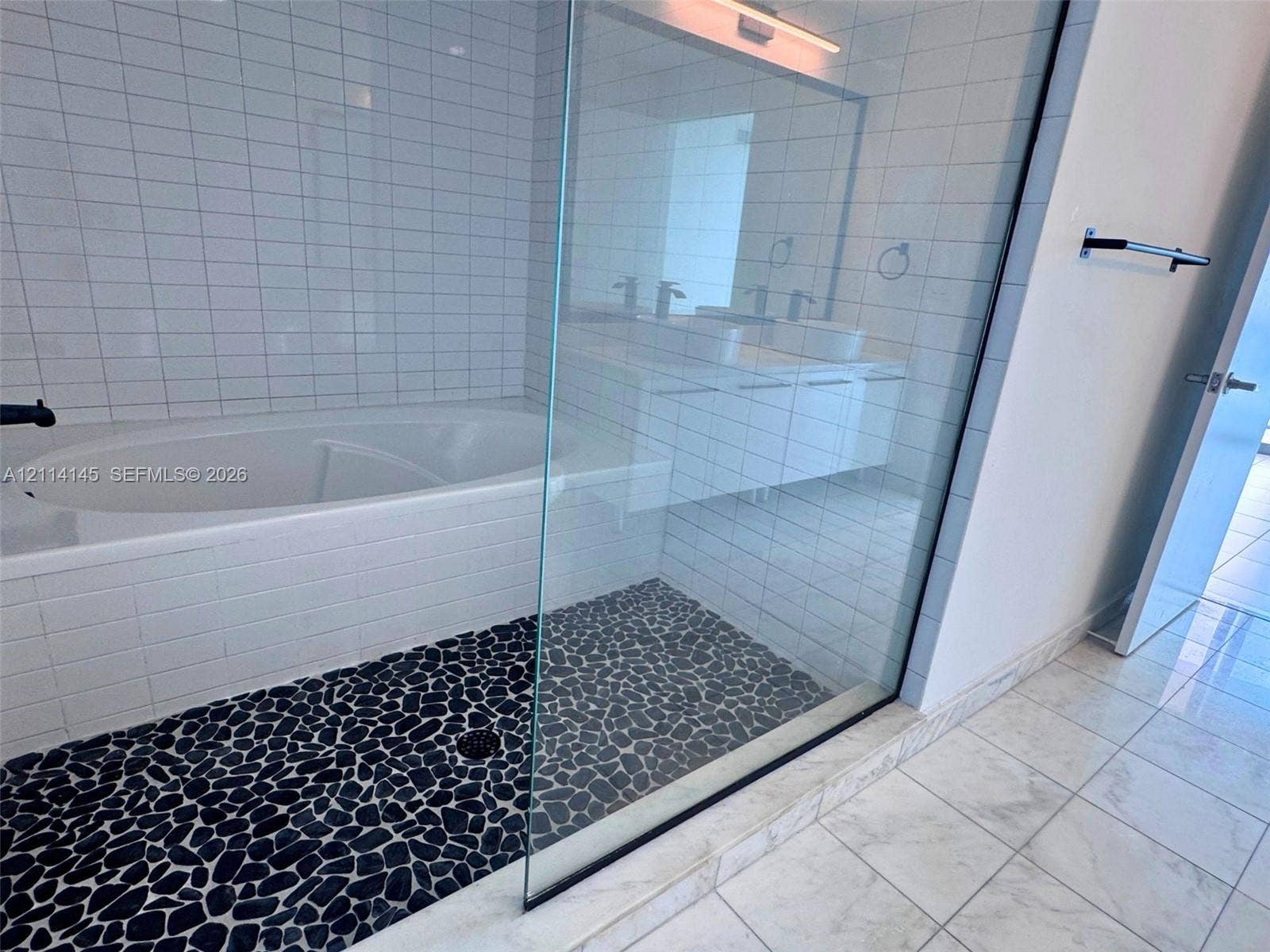 Large soaking tub, walk-in shower with river rock flooring, frameless glass enclosure, white tile wall finishes, and stone-tile flooring