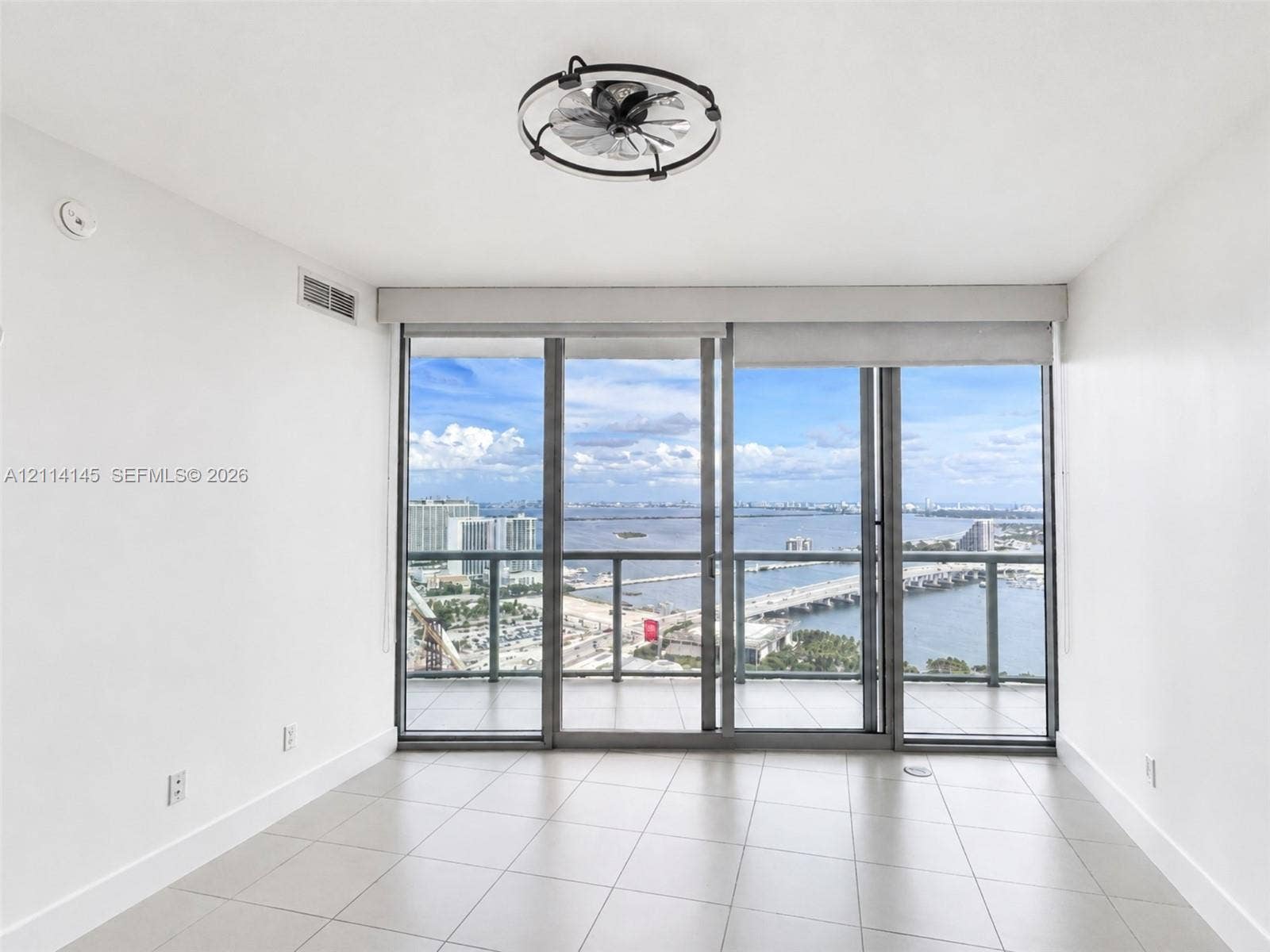 Floor-to-ceiling glass sliding doors, tile flooring, and a circular cage-style ceiling fan, featuring an expansive bay backdrop