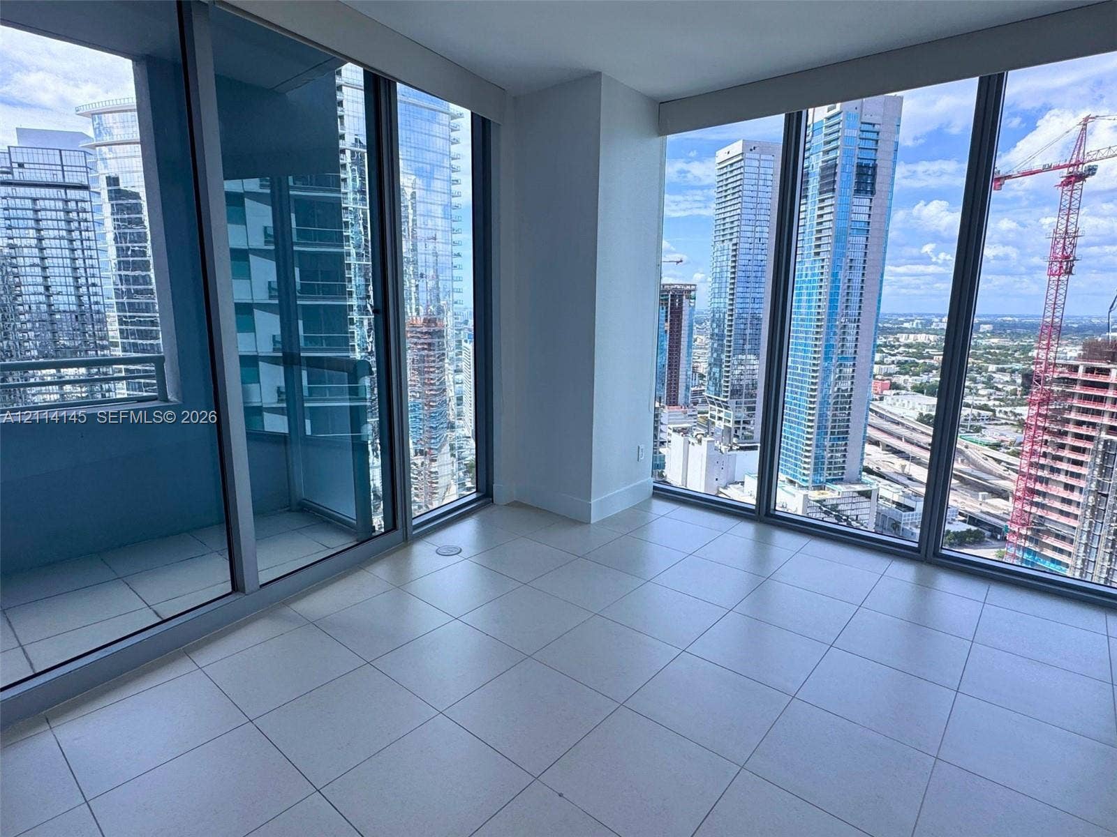 Floor-to-ceiling glass windows, expansive urban skyline imagery, neutral tile flooring, and sliding glass panel door