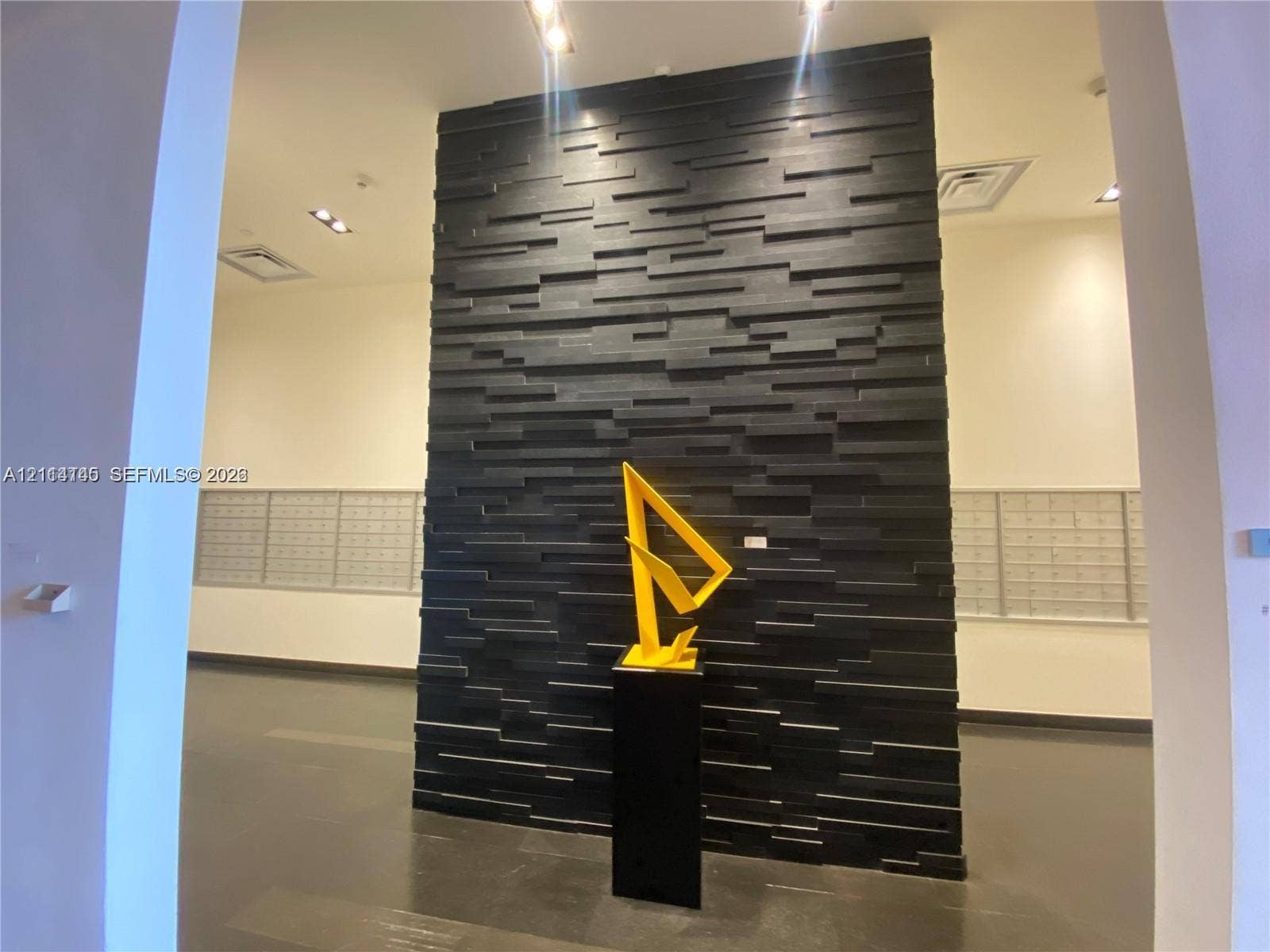 Textured black stone feature wall with recessed overhead accent lighting and metallic parcel storage units