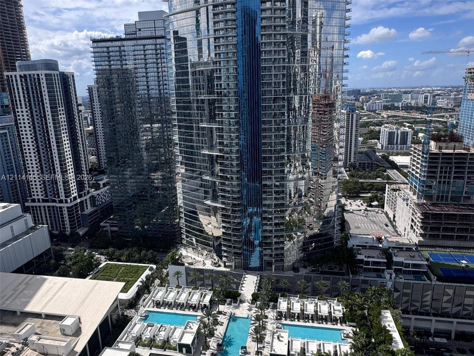 High-rise urban setting featuring tiered swimming pools, landscaped terrace areas with palm trees, and glass-faade architecture