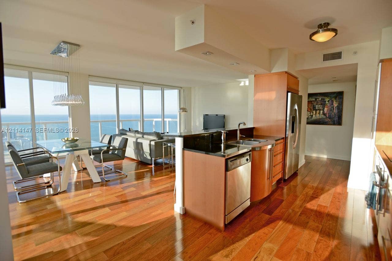 6365 Collins Avenue, #3908, Miami Beach, FL 33141 Wood-finish flooring, kitchen island with dark solid-surface countertop, stainless steel appliances, and floor-to-ceiling windows