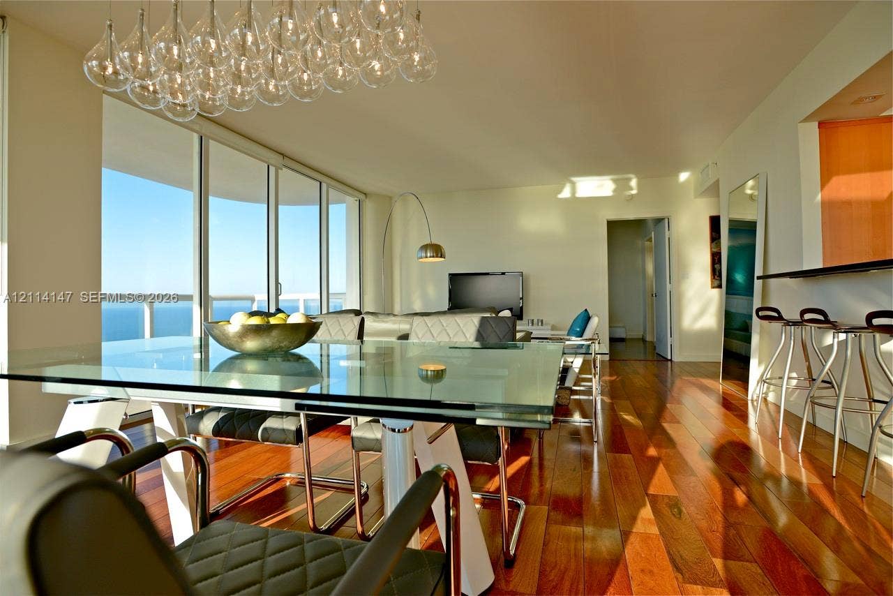 6365 Collins Avenue, #3908, Miami Beach, FL 33141 Floor-to-ceiling glass windows, wide-plank wood-finish flooring, custom multi-pendant chandelier, and a built-in breakfast bar