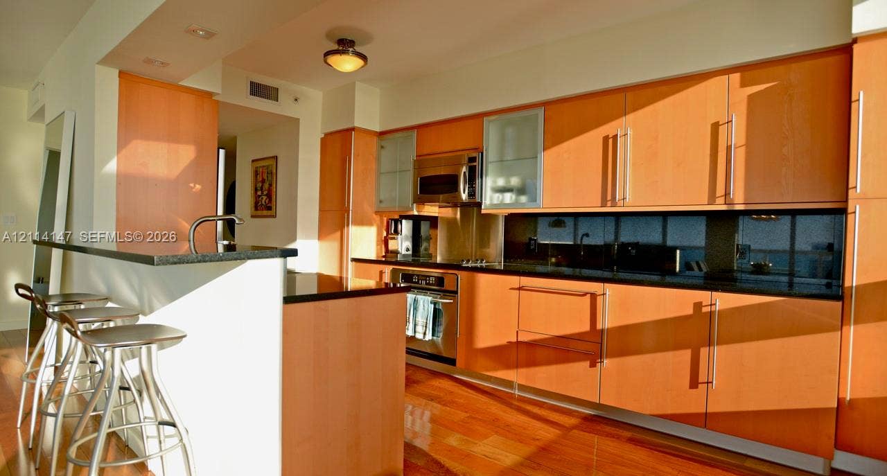 6365 Collins Avenue, #3908, Miami Beach, FL 33141 Kitchen featuring wood cabinetry, stainless steel appliances, dark stone-finish countertops, an integrated breakfast bar, and wood-finish flooring