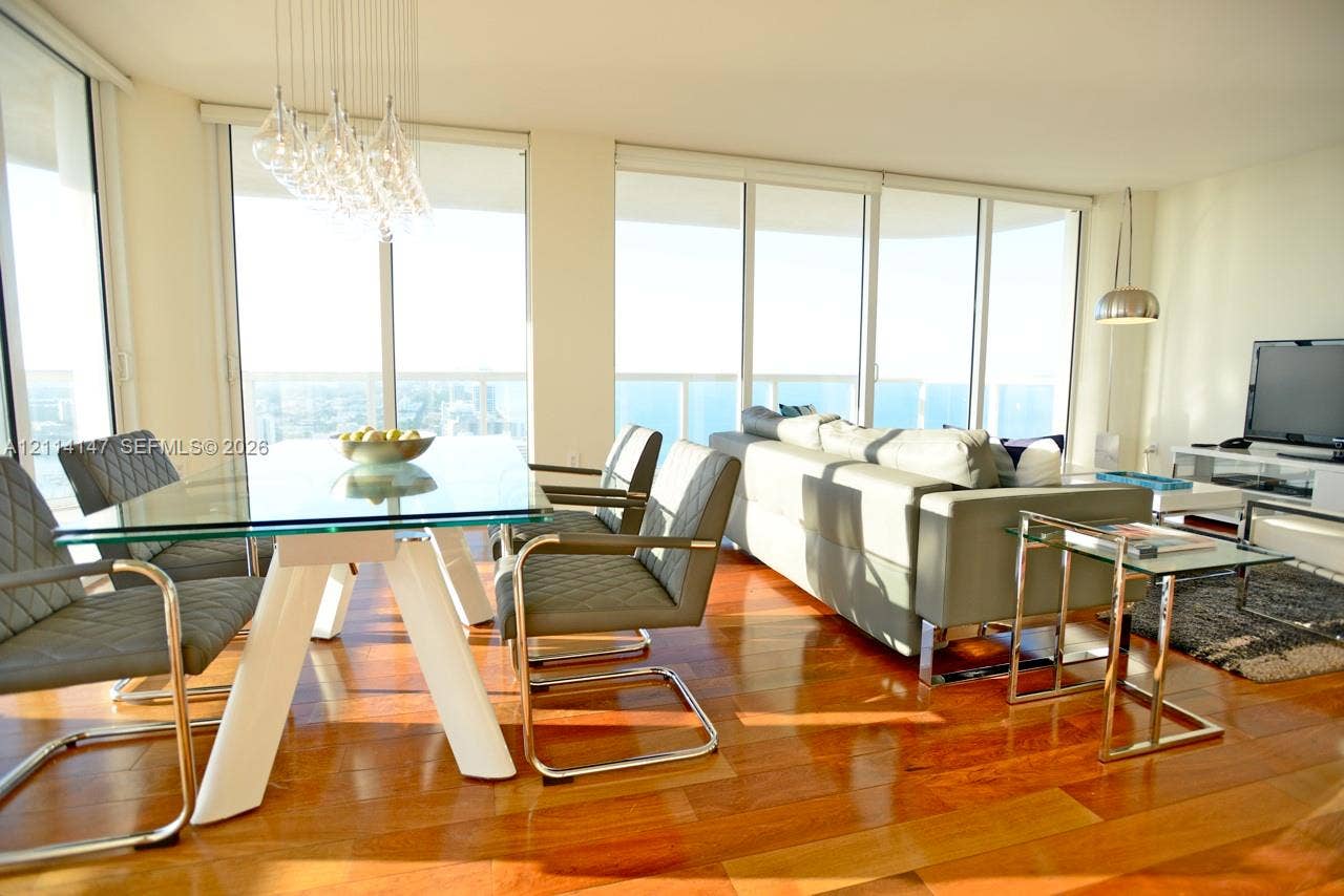 6365 Collins Avenue, #3908, Miami Beach, FL 33141 Open-concept interior featuring floor-to-ceiling windows, wood-finish flooring, and a contemporary multi-bulb chandelier