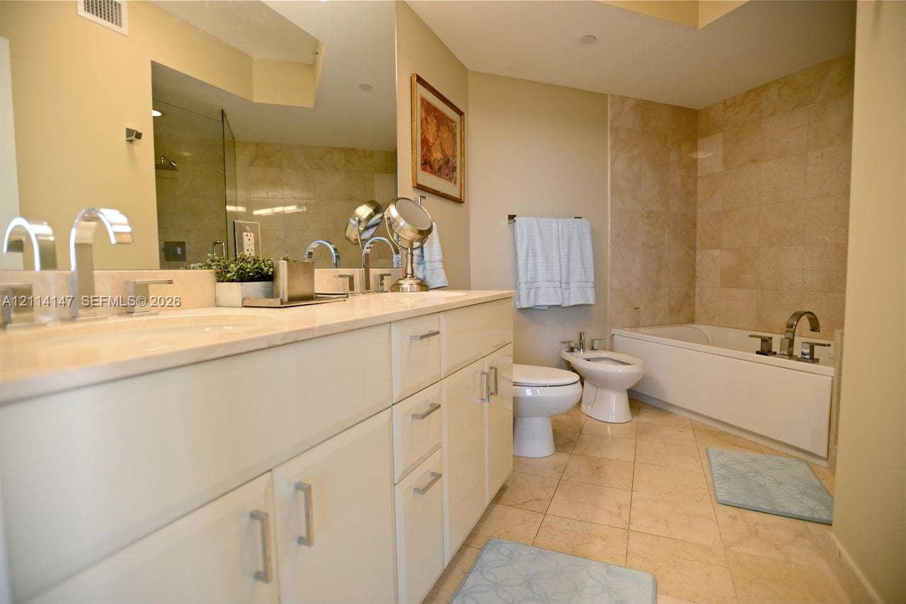 6365 Collins Avenue, #3908, Miami Beach, FL 33141 Double vanity with stone countertop, undermount sinks, and polished chrome faucets, featuring a full-width mirror, tile flooring, and a tiled shower-tub combination