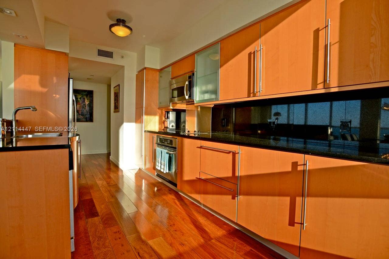 6365 Collins Avenue, #3908, Miami Beach, FL 33141 Kitchen featuring flat-panel wood cabinetry, black countertops, stainless steel appliances, and wood-finish flooring