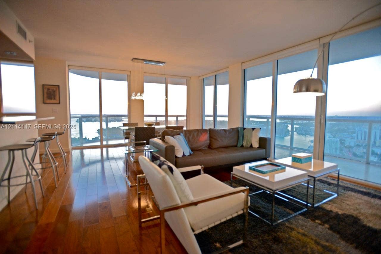 6365 Collins Avenue, #3908, Miami Beach, FL 33141 Open-concept interior featuring floor-to-ceiling glass walls, expansive water scenery, wood-finish flooring, and a built-in kitchen breakfast bar