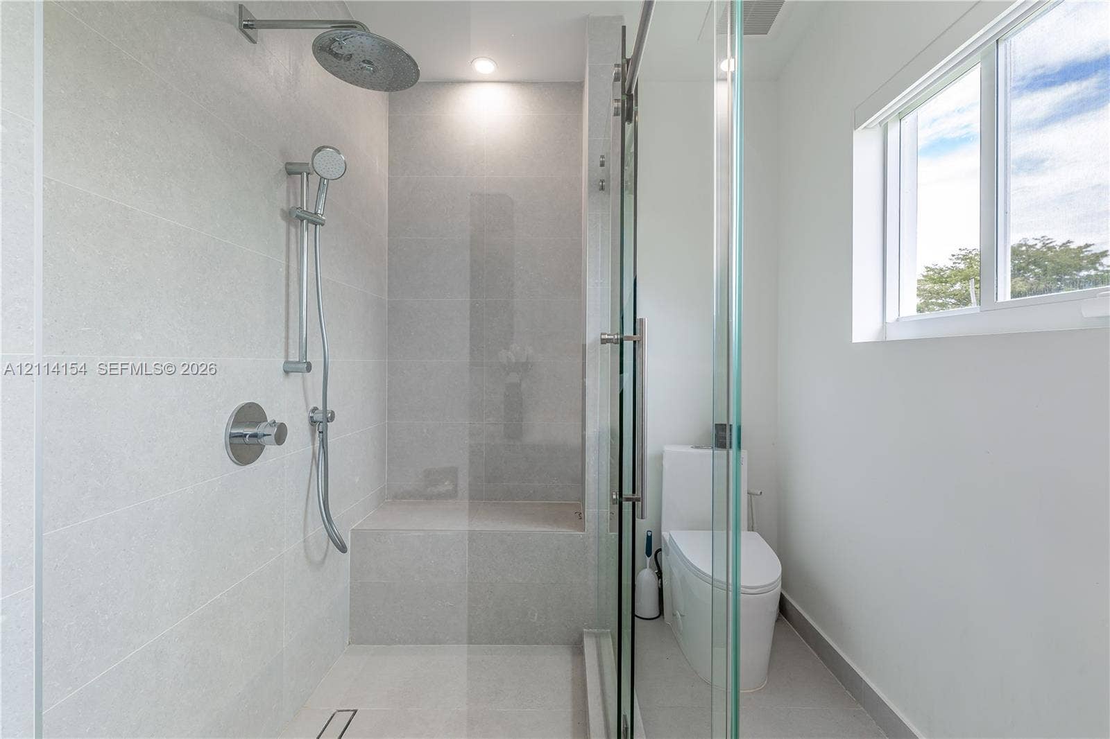 1126 NE 2nd Avenue, Fort Lauderdale, FL 33304 Walk-in shower with light-toned tiled surround, built-in tiled bench, rainfall shower head, adjustable handheld sprayer, and frameless glass enclosure